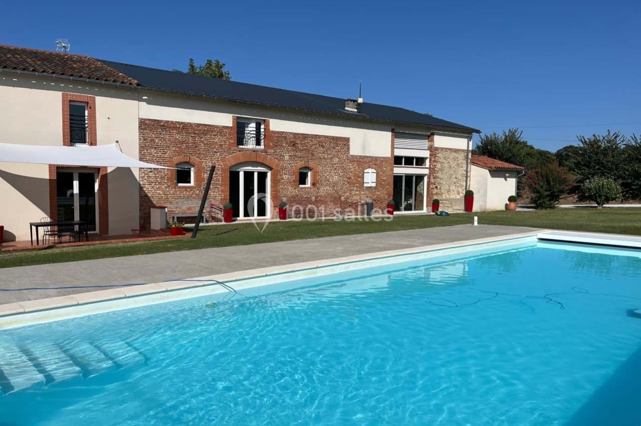 Bâtisse en briques rénovée avec piscine extérieure, pelouse et ciel dégagé en arrière-plan.