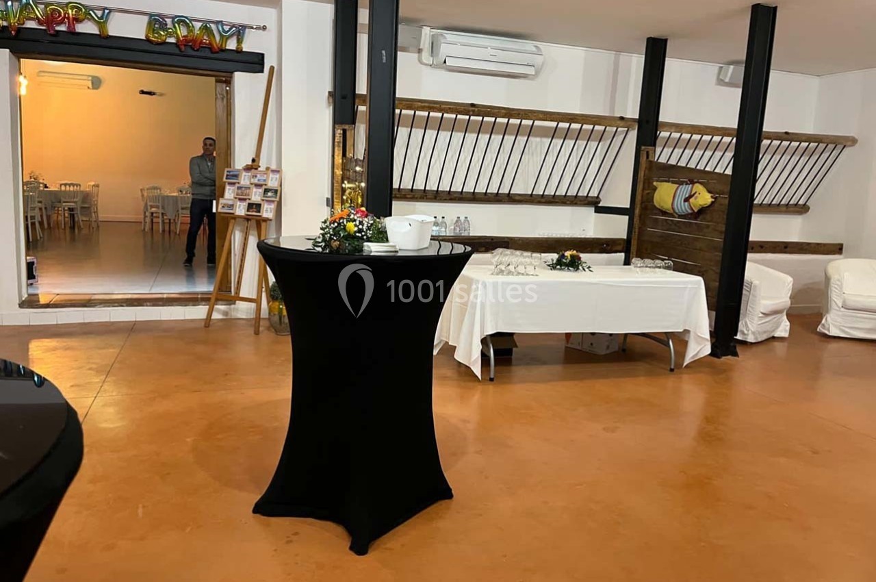 Salle de réception avec table haute noire au premier plan, buffet dressé et décorations murales en arrière-plan.