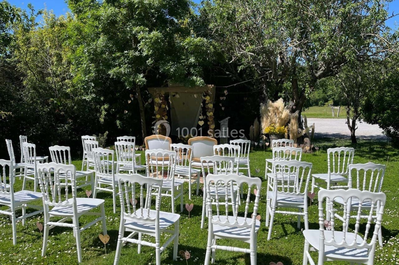 Chaises blanches disposées en rangées sur une pelouse, face à une arche décorée pour une cérémonie en plein air.