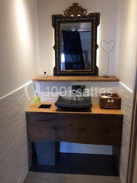 Lavabo moderne avec vasque noire sur meuble en bois, miroir encadré doré et accessoires décoratifs.
