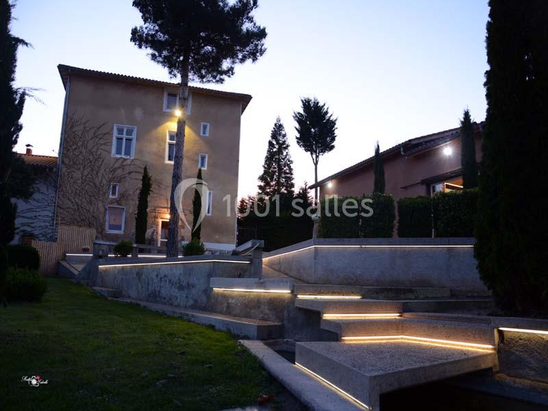 Escalier extérieur en pierre éclairé par des lumières LED, devant une maison au crépuscule avec des arbres environnants.