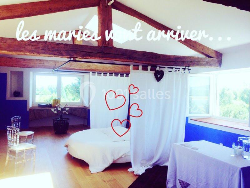 Chambre lumineuse avec poutres apparentes, lit décoré, rideaux blancs et vue sur l'extérieur verdoyant.