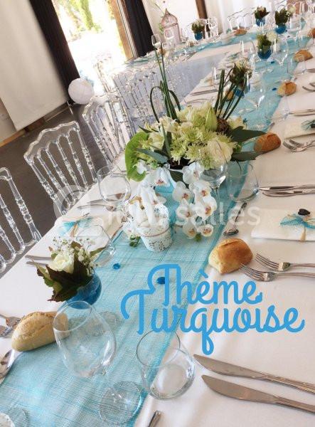 Table de réception décorée avec une nappe turquoise, des fleurs blanches et des chaises transparentes.