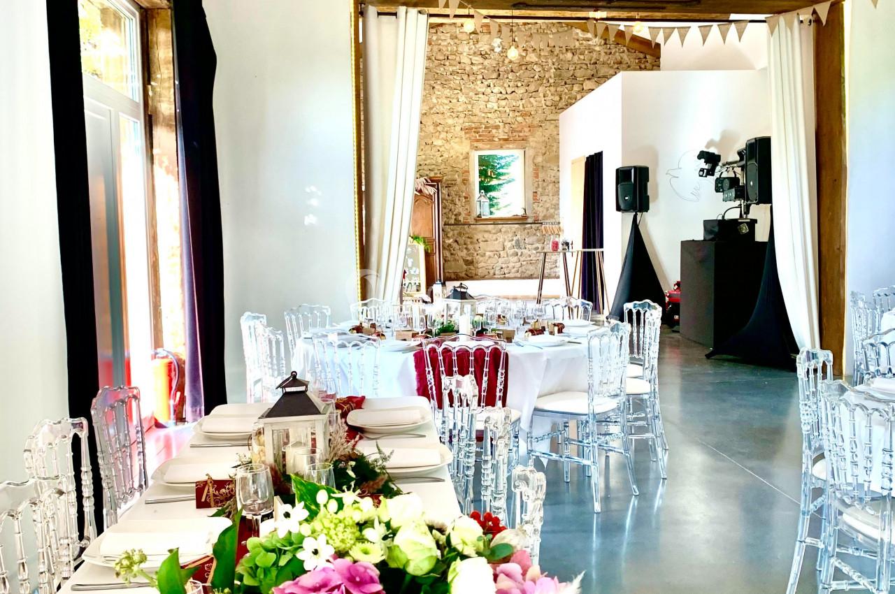 Salle de réception lumineuse décorée pour un événement, avec tables dressées, fleurs et guirlandes suspendues.