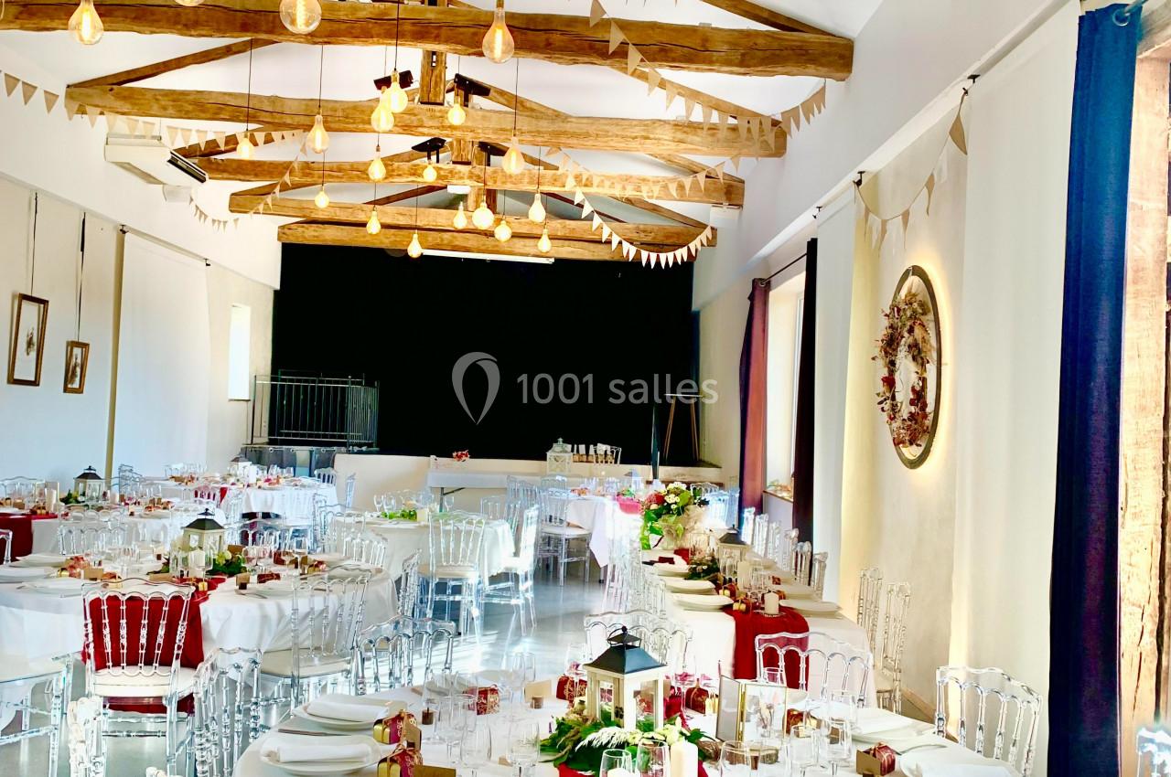 Salle de réception lumineuse avec tables rondes décorées de nappes blanches et rouges, guirlandes suspendues au plafond.