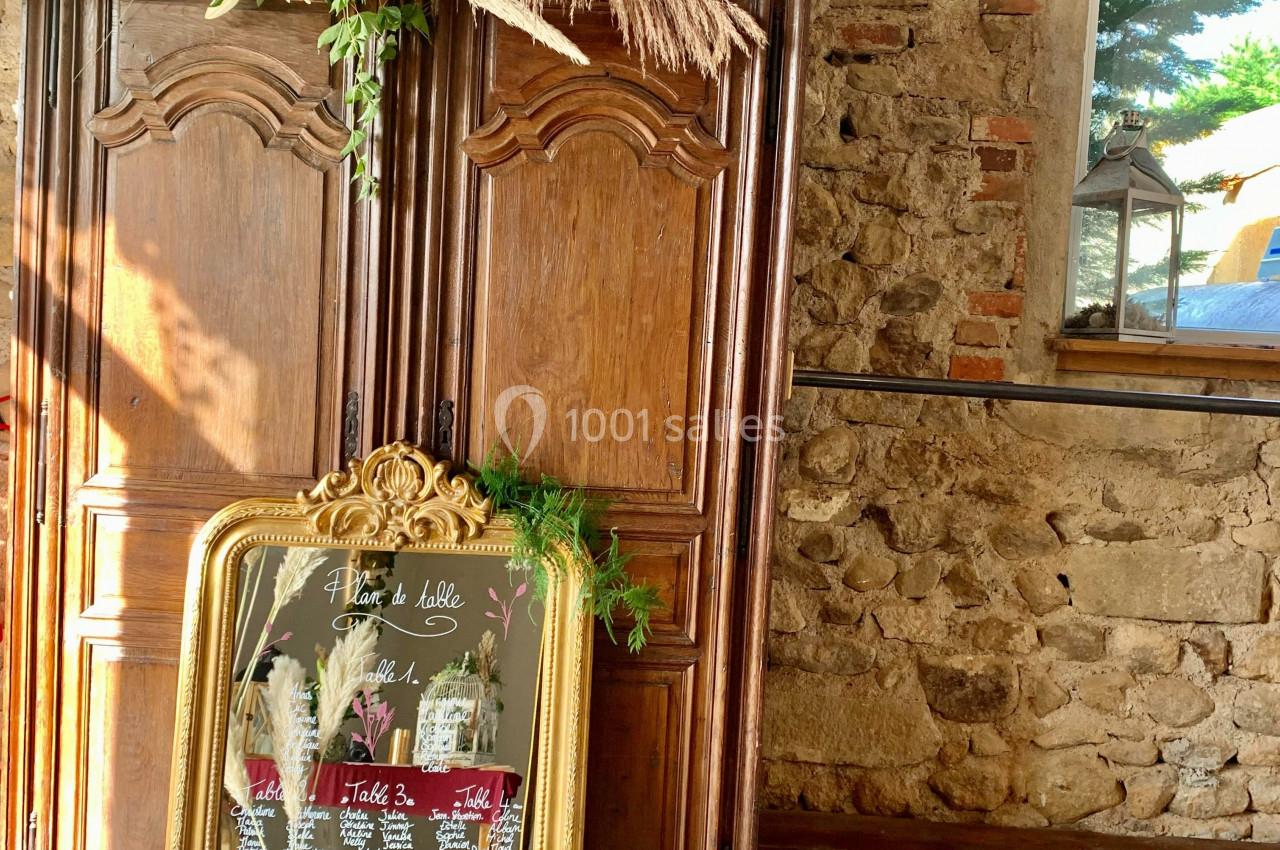 Armoire en bois rustique avec un plan de table encadré doré, décoré de plantes et pampas, dans une pièce en pierre.