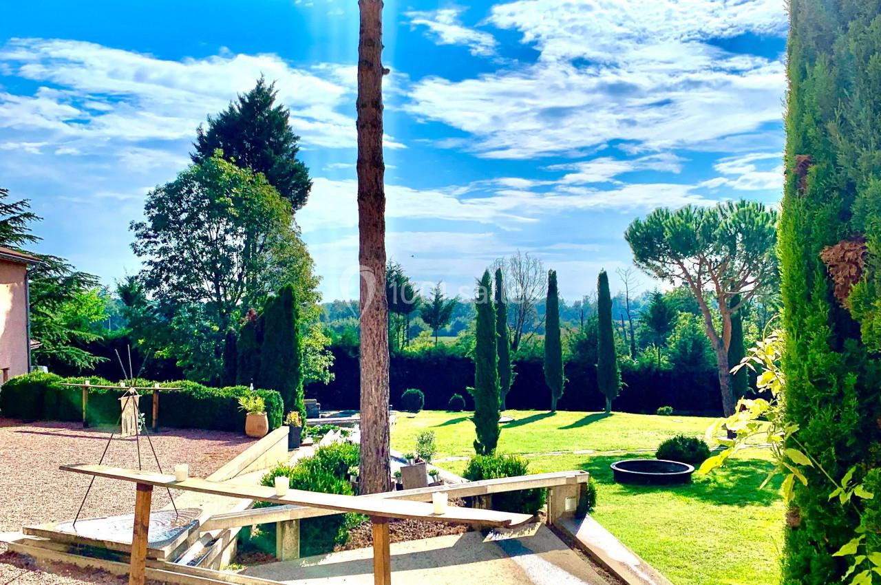 Jardin paysager avec pelouse, arbres taillés, bassin d'eau et ciel bleu en arrière-plan.