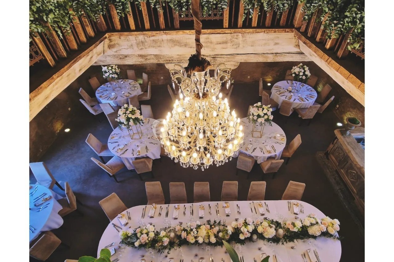 Vue plongeante sur une salle de réception élégante avec tables rondes et rectangulaires décorées de fleurs, sous un grand…