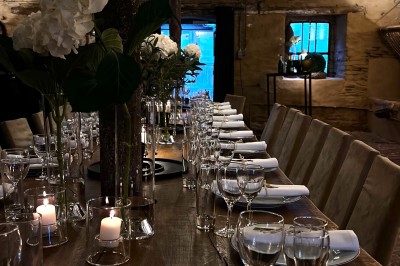 Cour pavée d'un bâtiment en pierre éclairé par des lumières extérieures, entouré d'arbres et de bâtiments annexes, de nuit.