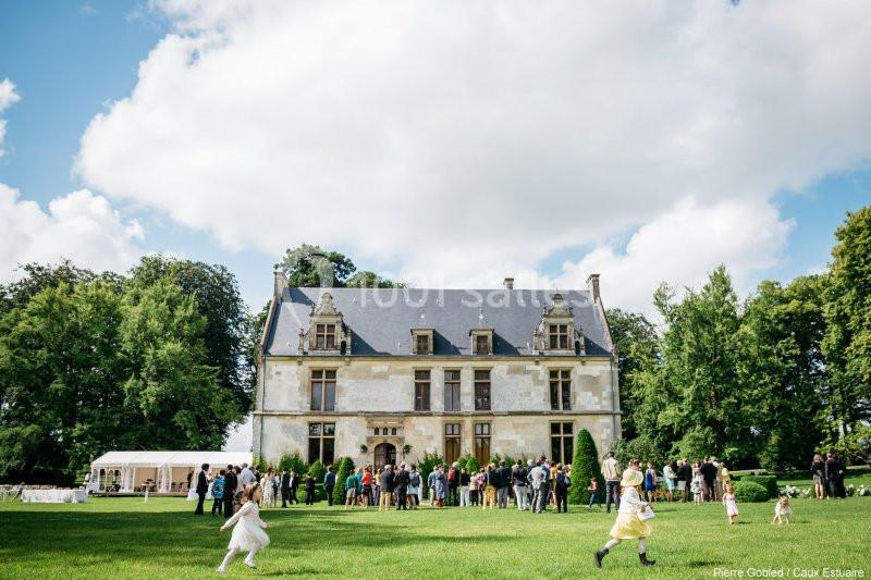 Groupe de personnes rassemblées devant un manoir ancien entouré de pelouse et d'arbres par une journée ensoleillée.