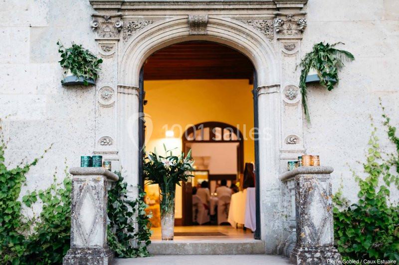 Entrée voûtée en pierre ornée de feuillages, donnant sur un intérieur éclairé avec des personnes en arrière-plan.