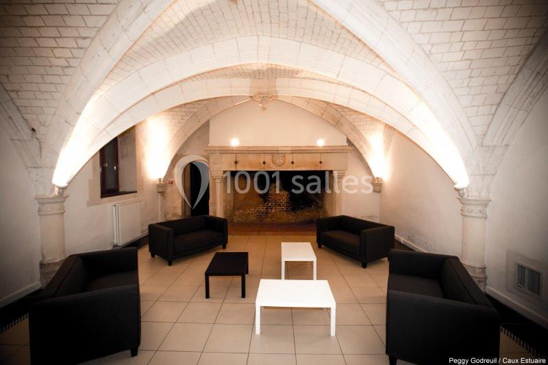 Salle voûtée avec cheminée ancienne, mobilier moderne comprenant canapés noirs et tables basses blanches.