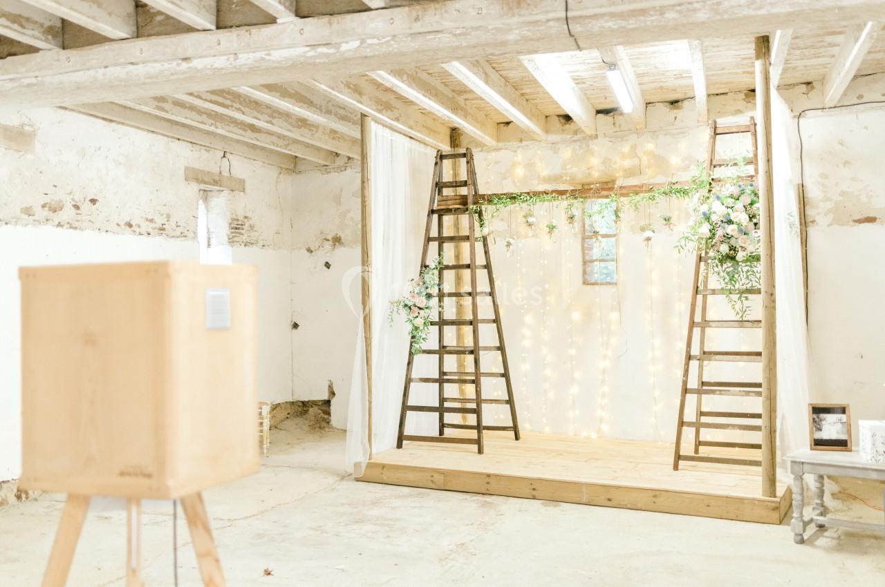 Scène de mariage rustique avec échelle en bois, guirlandes lumineuses et décor floral dans un espace en pierre.