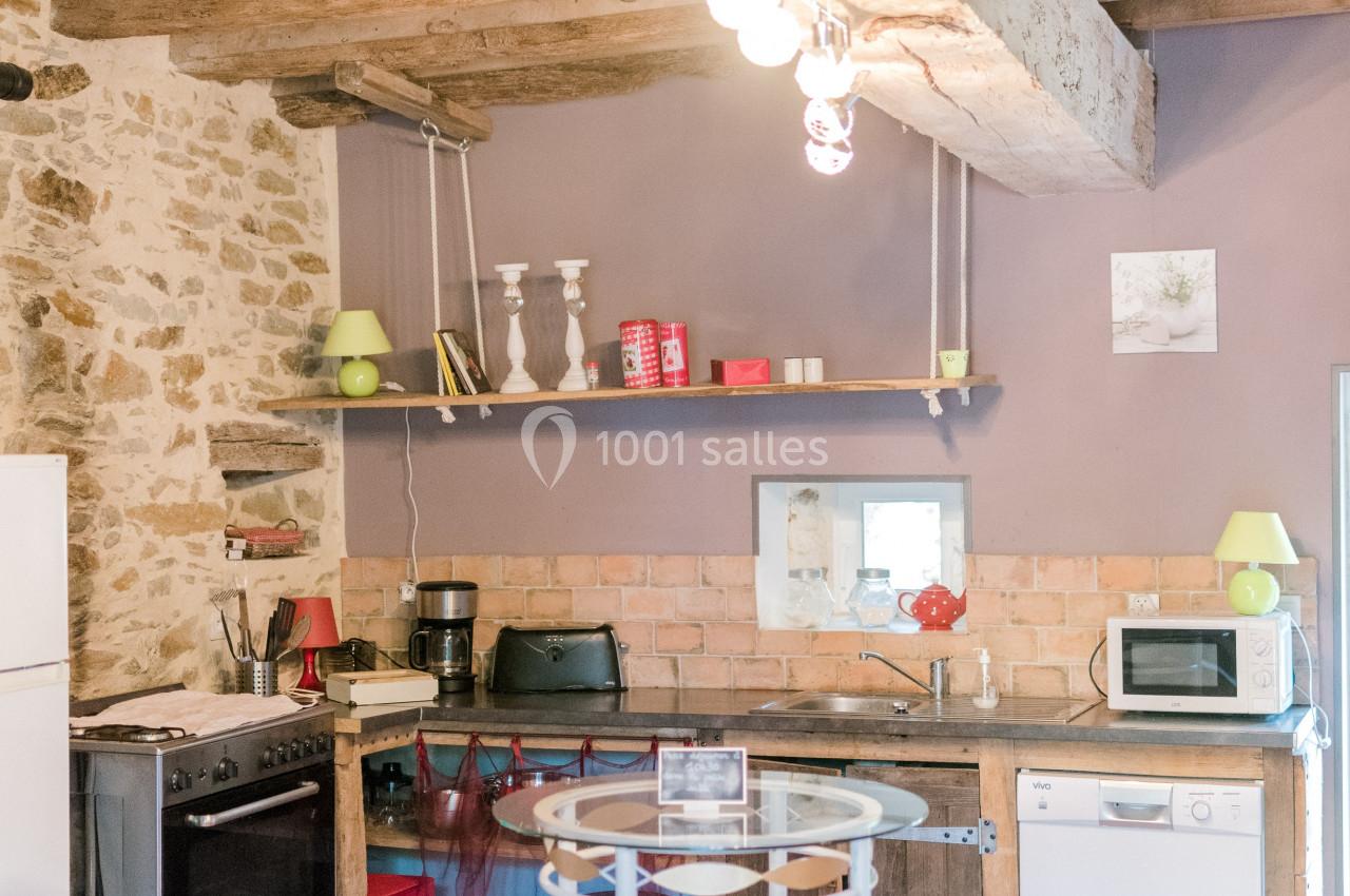 Cuisine rustique avec poutres apparentes, murs en pierre, électroménagers modernes et table ronde avec tabourets.