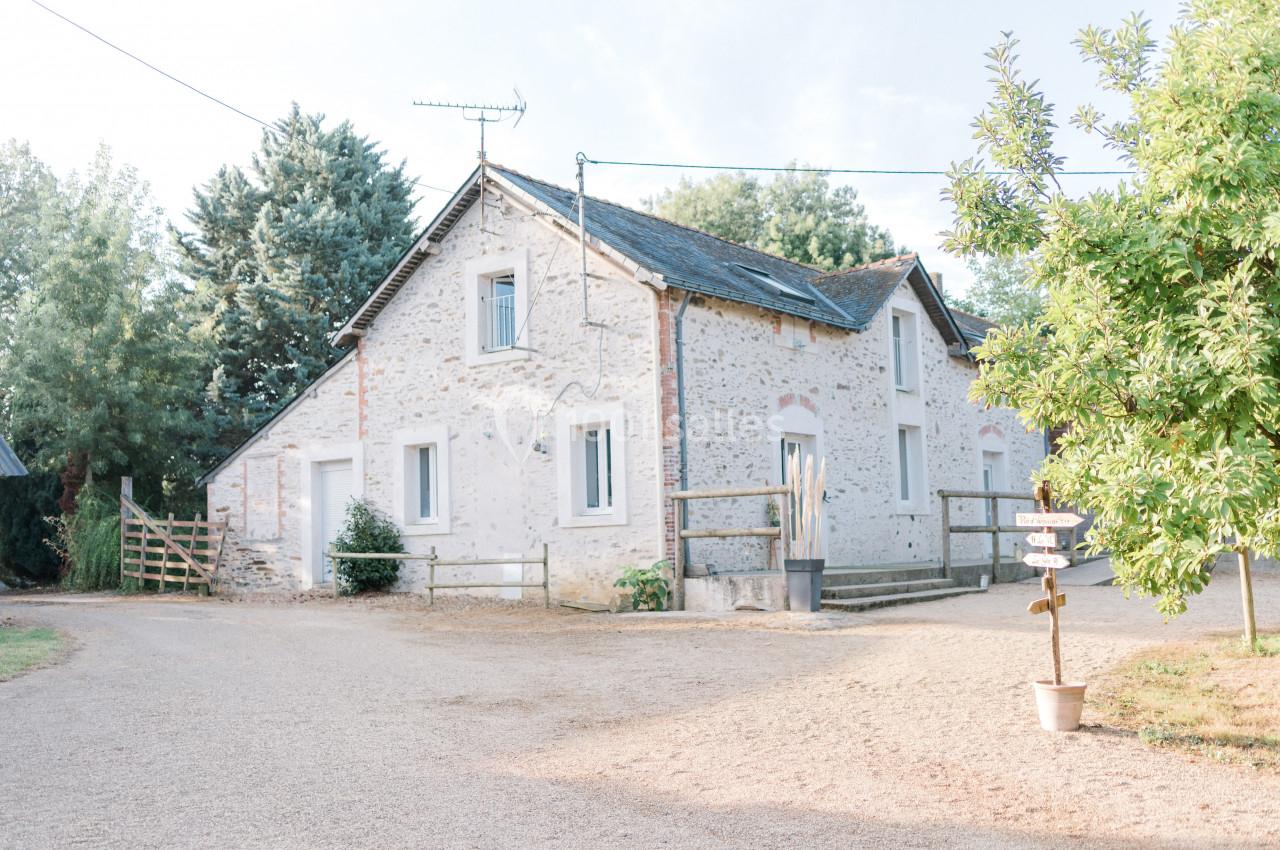 Maison en pierre blanche avec toit en ardoise, entourée d'arbres et située sur un chemin de gravier.