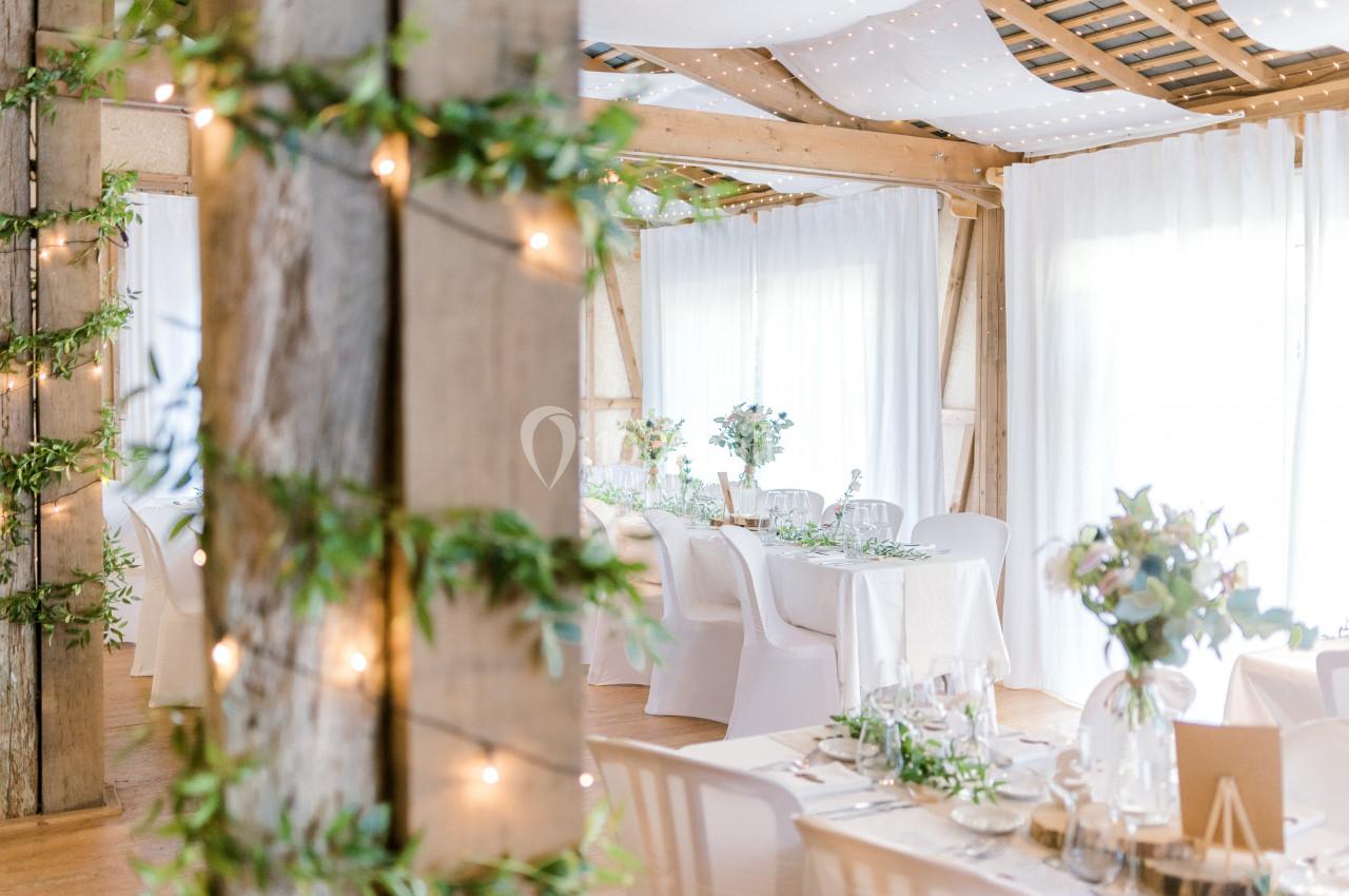 Salle de réception lumineuse décorée de guirlandes, de verdure et de tables dressées avec des fleurs.