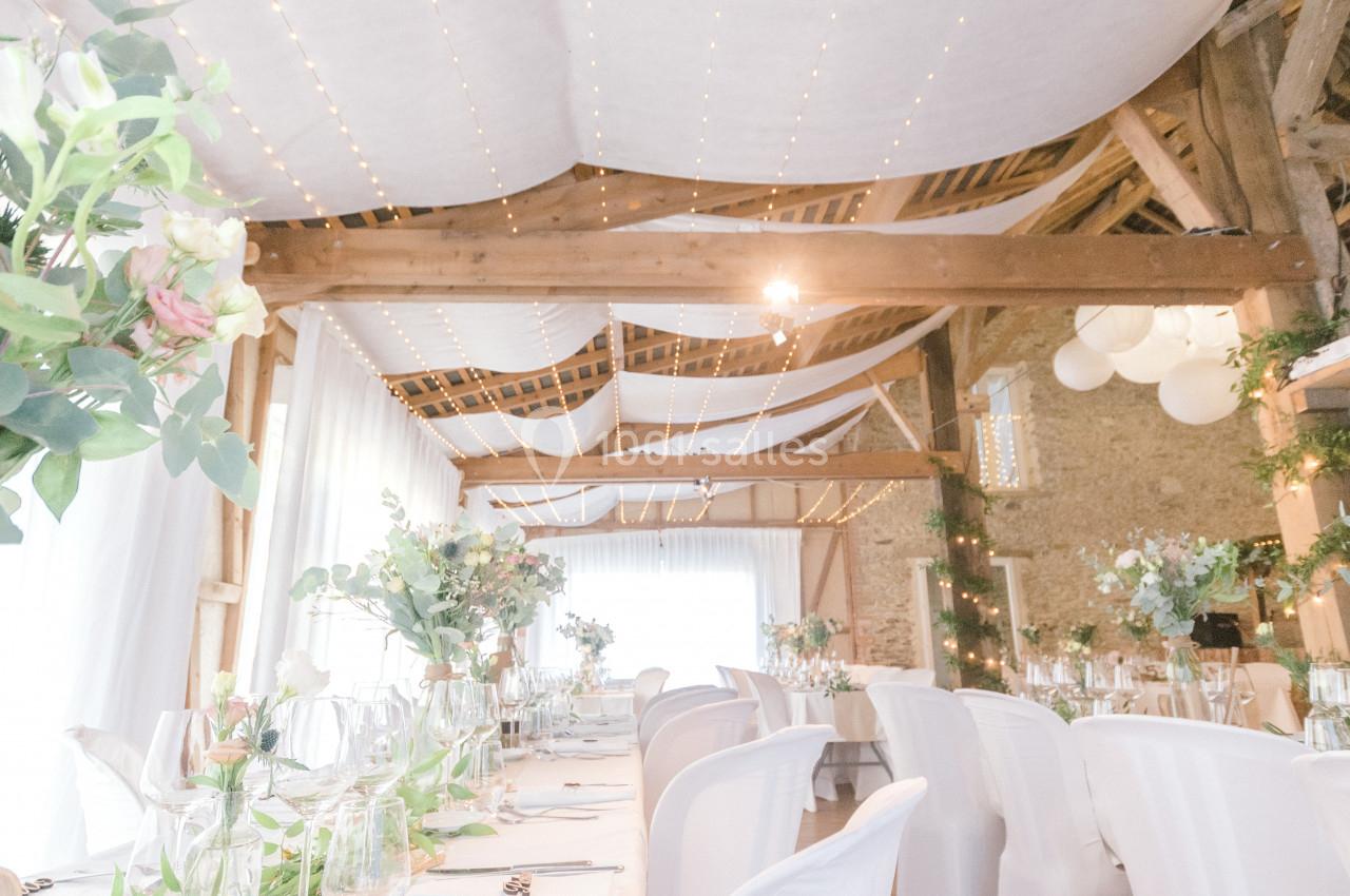Salle de réception lumineuse décorée avec des guirlandes lumineuses, des fleurs et des tables dressées pour un événement.