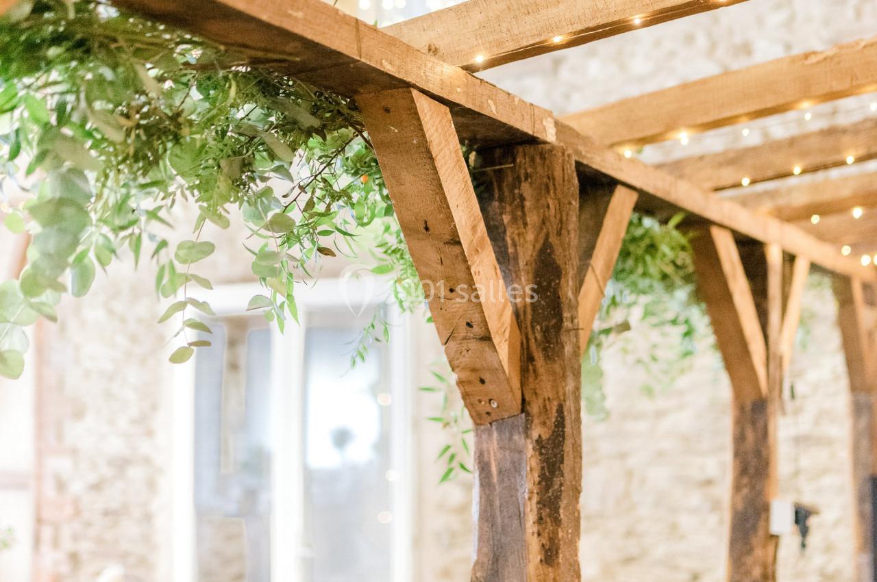 Structure en bois décorée de guirlandes lumineuses et de feuillage, dans une salle aux murs en pierre.
