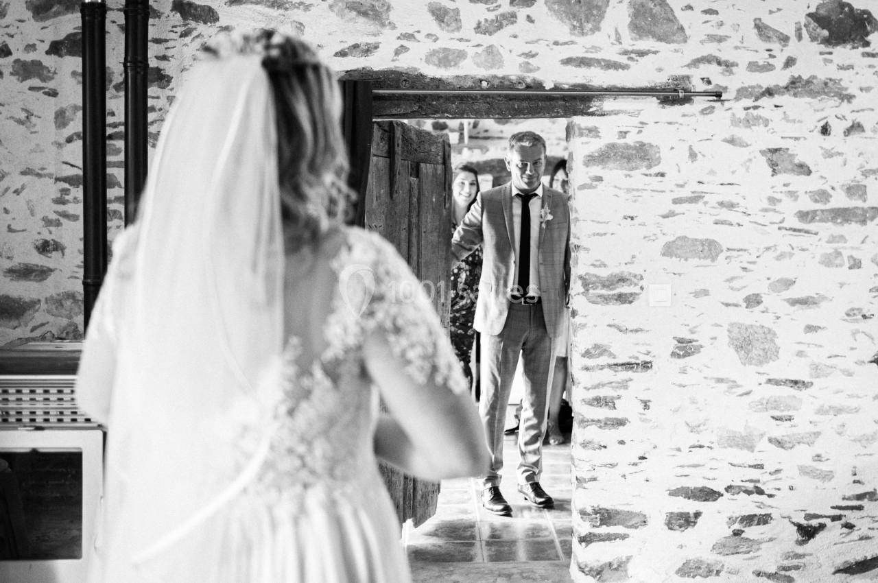 Une mariée de dos regarde un homme en costume entrant dans une pièce en pierre, visiblement ému.