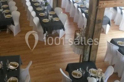 Salle de réception avec tables dressées, nappes noires, chaises blanches et parquet en bois clair.