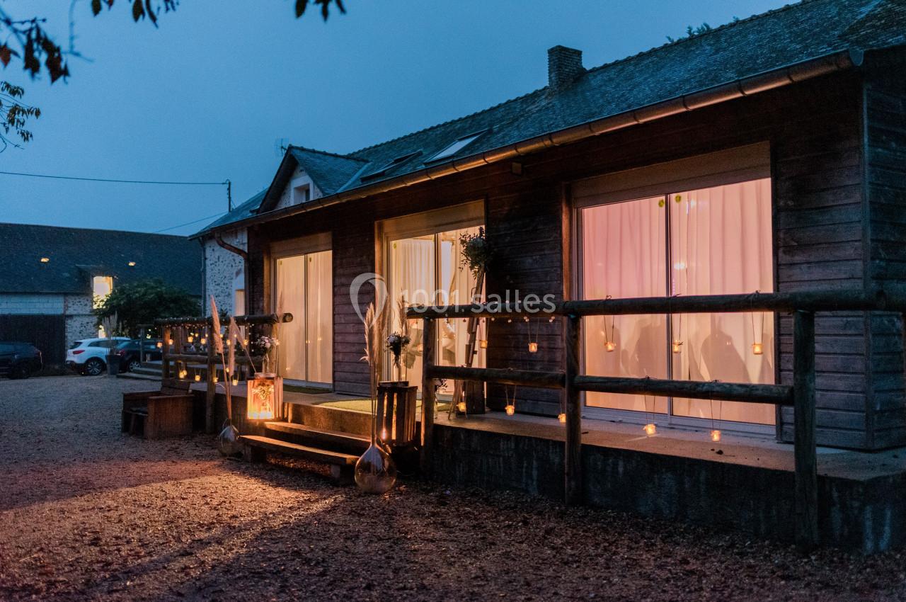 Maison en bois éclairée à la tombée de la nuit, avec des bougies et des décorations lumineuses sur la terrasse.