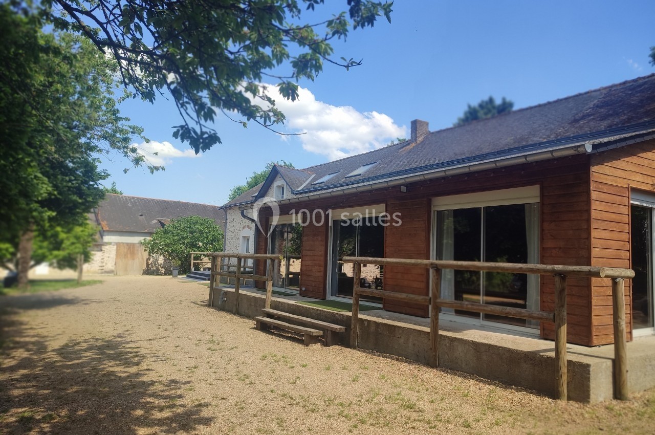 Maison en bois avec terrasse, entourée d'arbres, sous un ciel bleu dégagé.