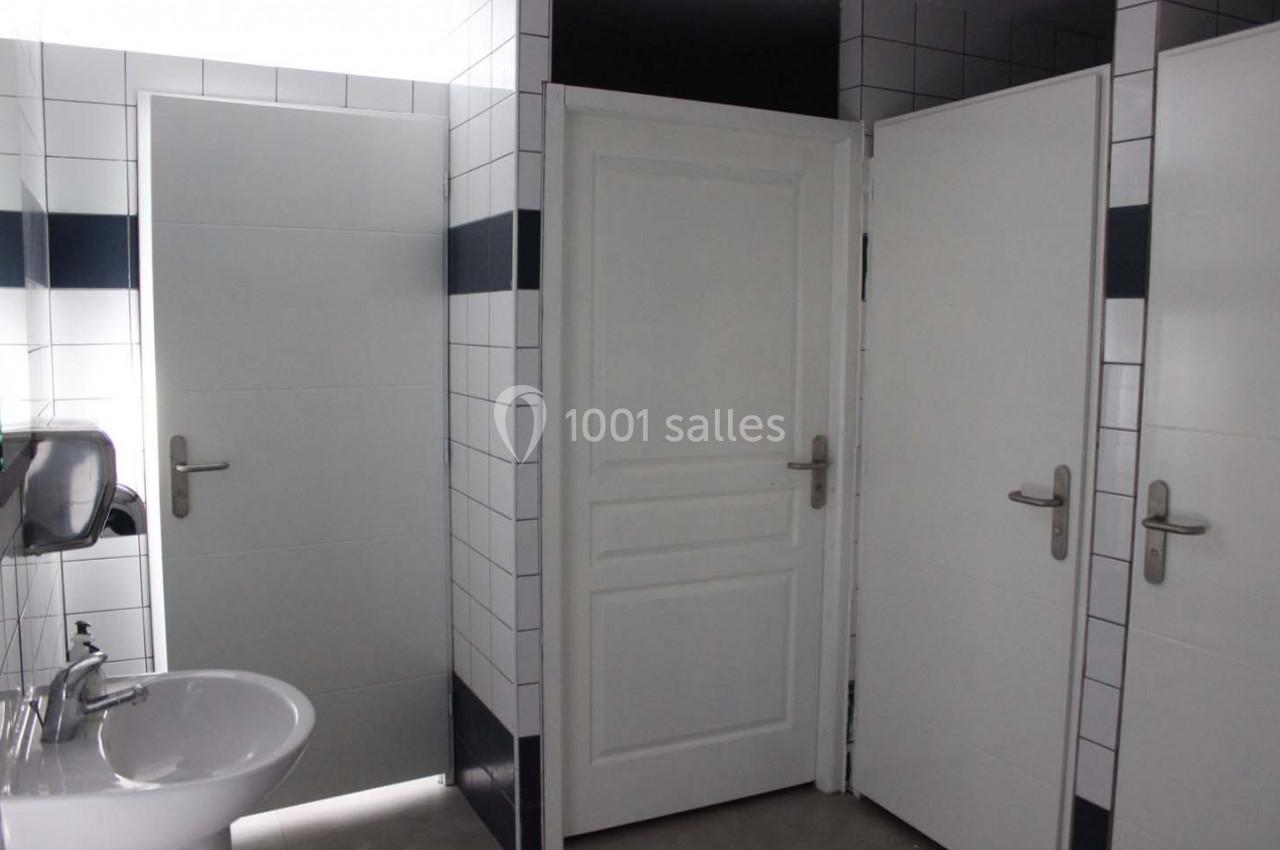 Portes de cabines de toilettes blanches dans un espace carrelé avec un lavabo et un distributeur de savon.