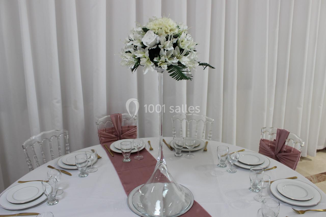 Centre de table avec vase haut et bouquet de fleurs blanches, entouré d'une table dressée avec vaisselle élégante.