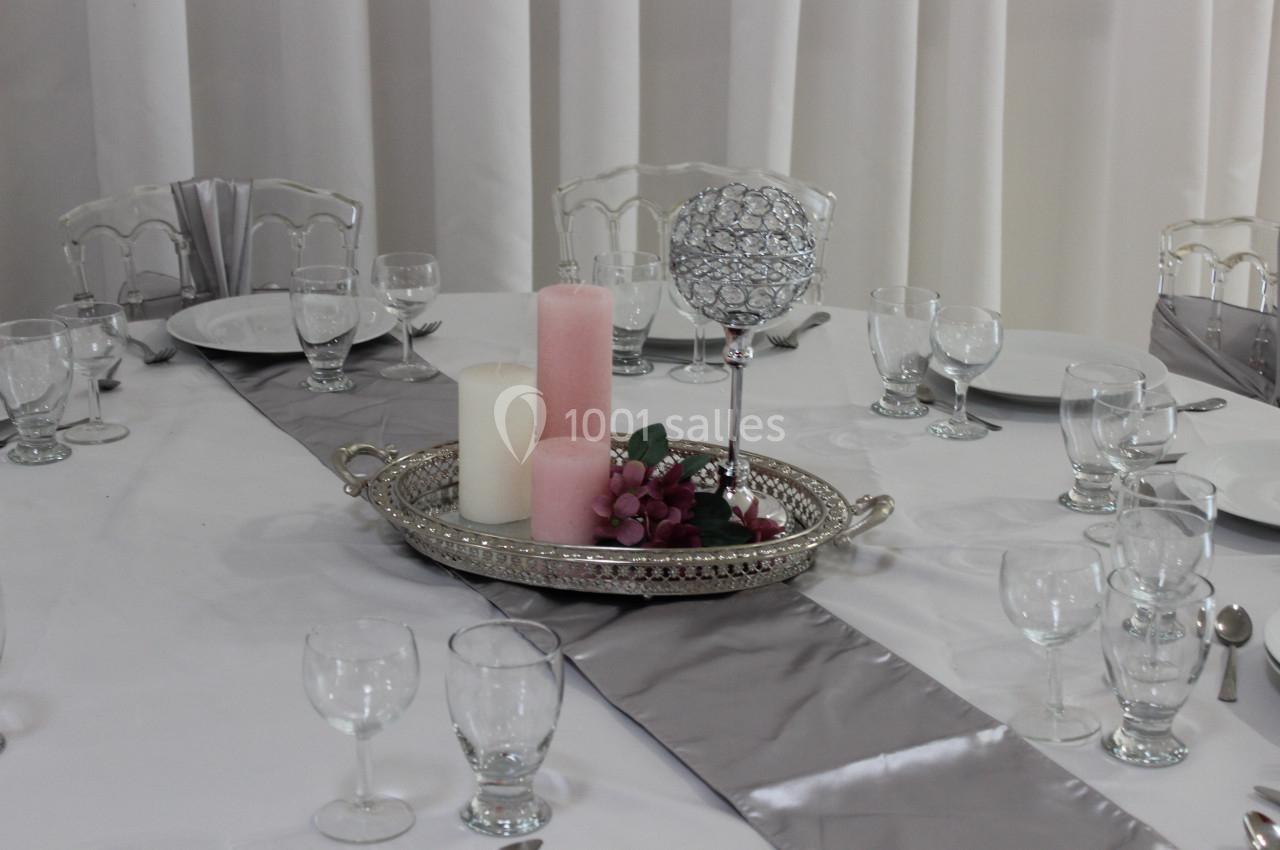 Table dressée avec nappe blanche, chemins de table gris, bougies et décoration florale sur un plateau argenté.