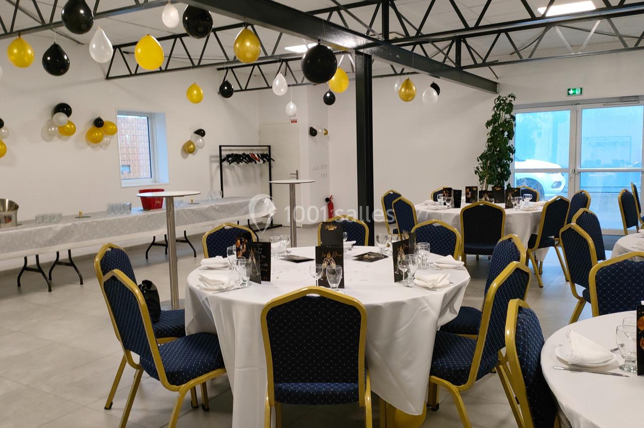 Salle décorée pour un événement avec des tables rondes dressées, des ballons noirs et jaunes, et un buffet en arrière-plan.