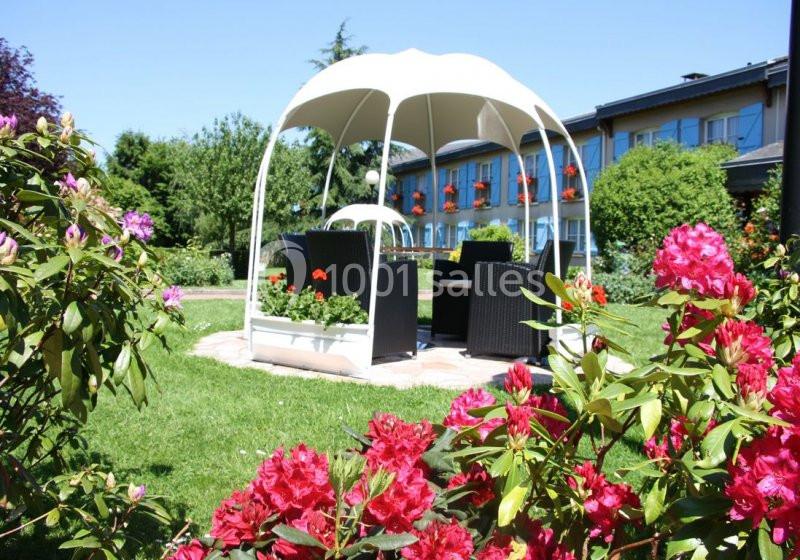 Tonnelle blanche avec mobilier de jardin noir, entourée de fleurs colorées dans un espace vert ensoleillé.