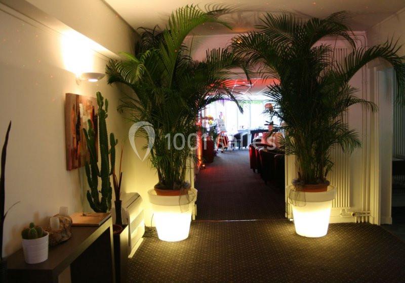 Couloir décoré de plantes en pot et éclairé par des lumières tamisées, menant à une salle animée.