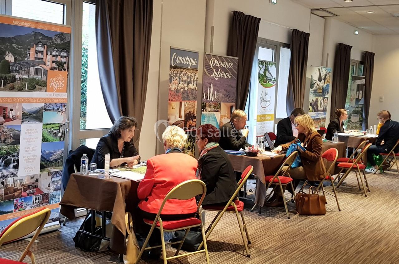 Des personnes discutent en face à face à des tables dans une salle avec des affiches promotionnelles en arrière-plan.