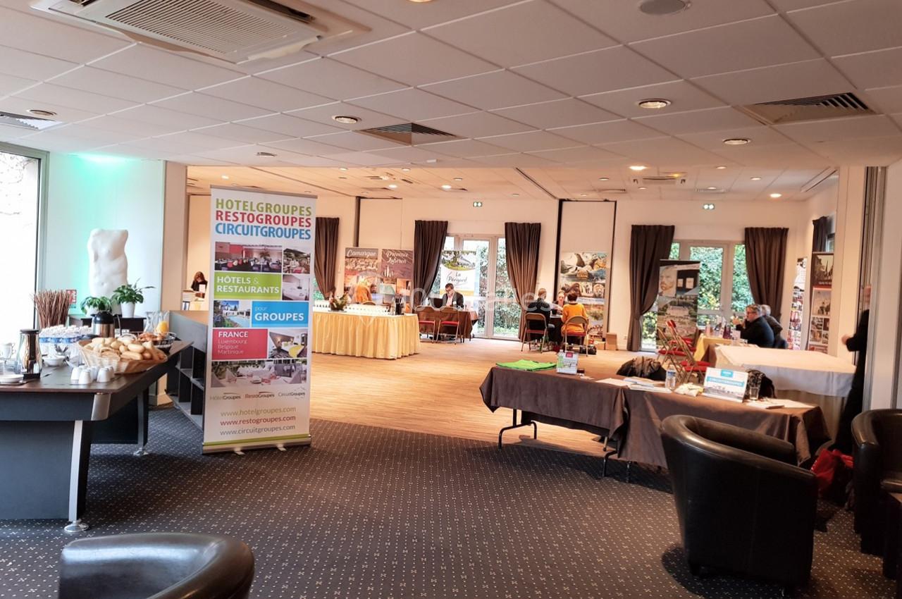 Salle d'exposition avec stands promotionnels, brochures et tables, éclairée par des baies vitrées.