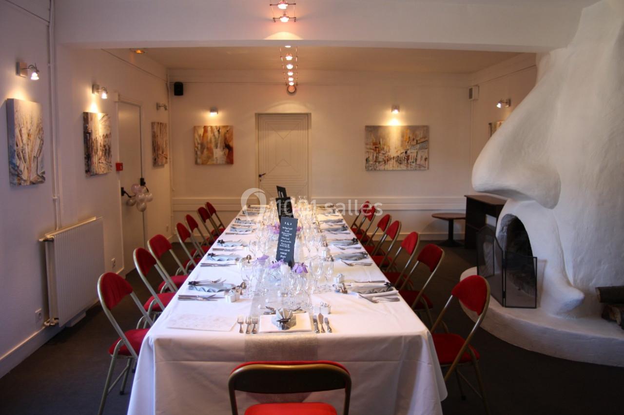 Salle de réception avec une grande table dressée, entourée de chaises rouges, et décorée de peintures murales.