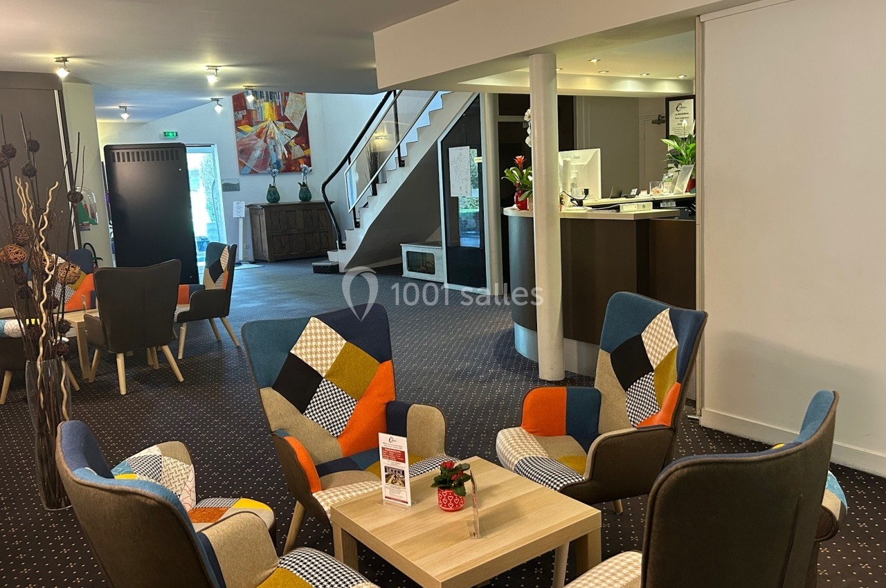 Location salle Saint-Martin-du-Vivier (Seine-Maritime) - The Originals Relais La Bertelière - Rouen #2 Espace d'accueil lumineux avec fauteuils colorés, table basse, comptoir de réception et escalier en arrière-plan.