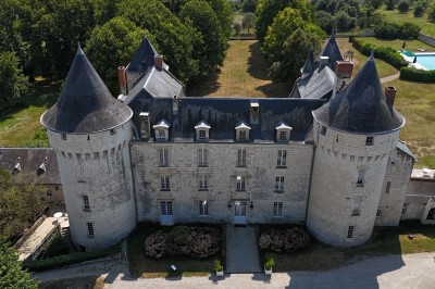 Chambre avec lit double, canapé, table basse et poutres apparentes, décorée de papier peint à motifs.