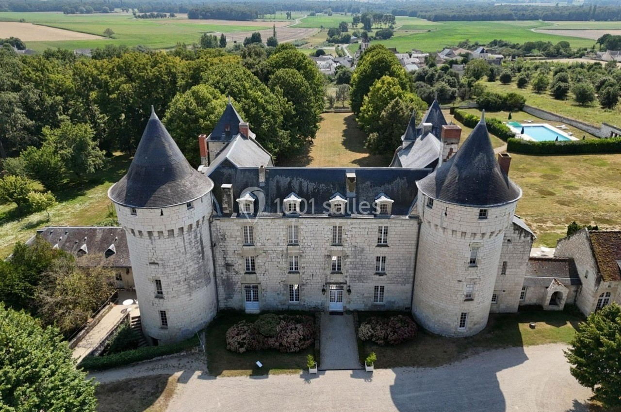 Vue aérienne d'un château en pierre avec quatre tours, entouré de jardins, d'arbres et d'une campagne verdoyante.