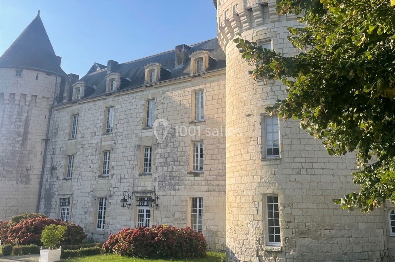 Façade d'un château en pierre blanche avec tours rondes, fenêtres alignées et jardin fleuri au premier plan.