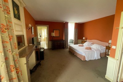 Chambre avec lit double, canapé, table basse et poutres apparentes, décorée de papier peint à motifs.