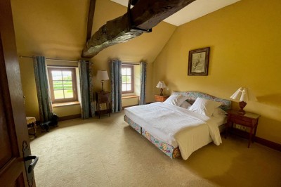 Chambre avec lit double, canapé, table basse et poutres apparentes, décorée de papier peint à motifs.