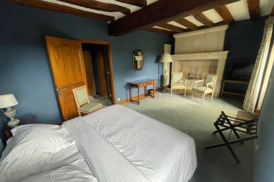 Chambre avec lit double, canapé, table basse et poutres apparentes, décorée de papier peint à motifs.