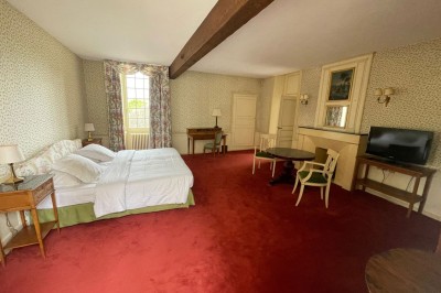 Chambre avec lit double, canapé, table basse et poutres apparentes, décorée de papier peint à motifs.