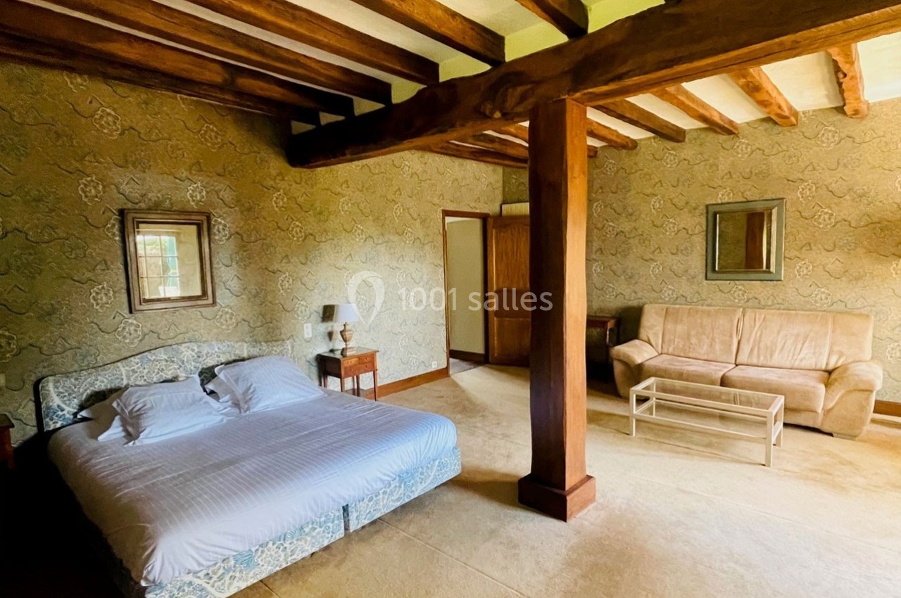 Chambre avec lit double, canapé, table basse et poutres apparentes, décorée de papier peint à motifs.