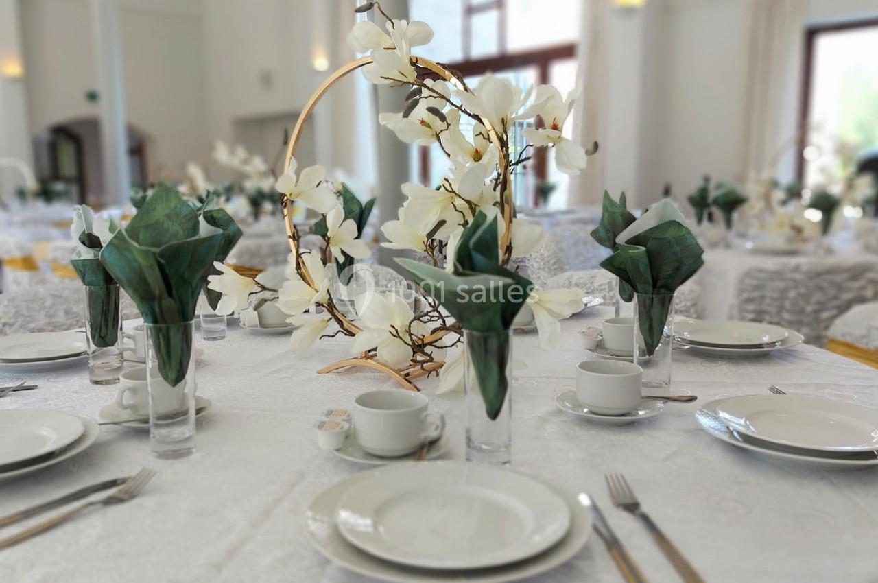 Table dressée avec vaisselle blanche, serviettes pliées, et centre de table floral dans une salle lumineuse.