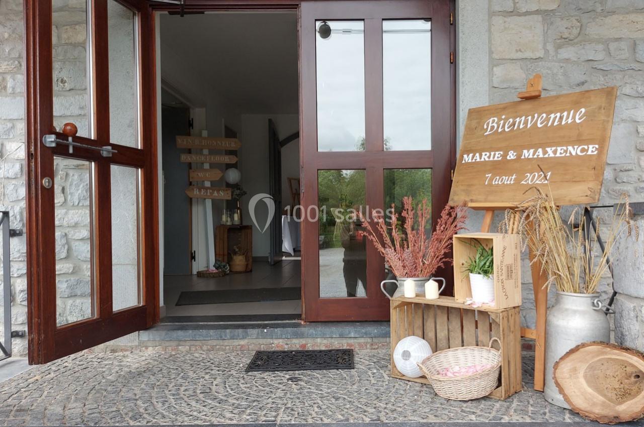 Entrée d'un bâtiment en pierre décorée avec un panneau de bienvenue, des fleurs séchées et des objets rustiques.
