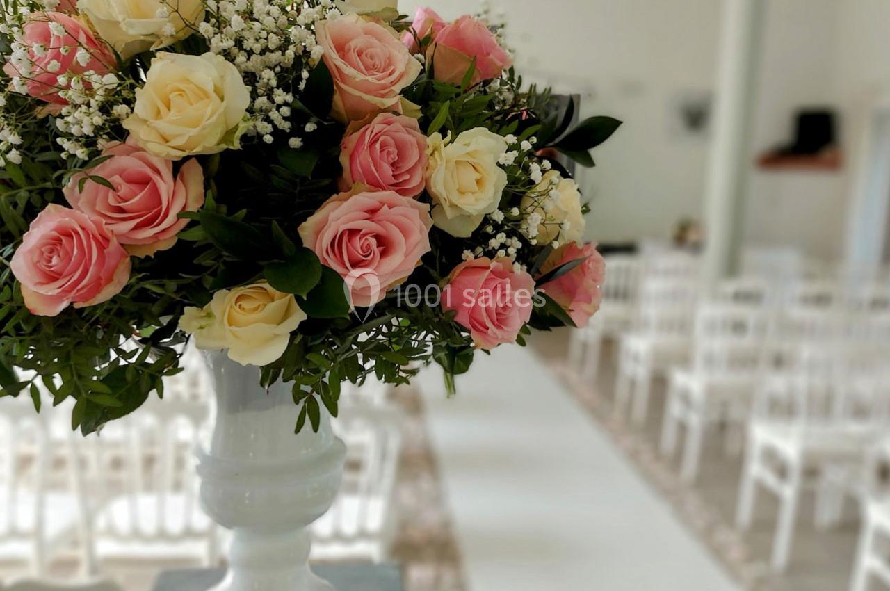 Bouquet de roses roses et blanches avec gypsophile dans un vase blanc, placé dans une salle décorée pour un événement.