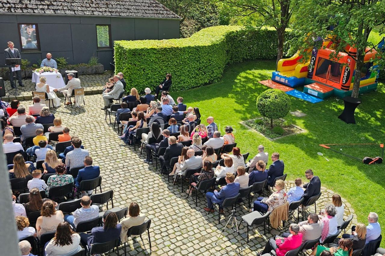 Cérémonie en plein air avec des invités assis, un officiant, une table décorée et une structure gonflable en arrière-plan.