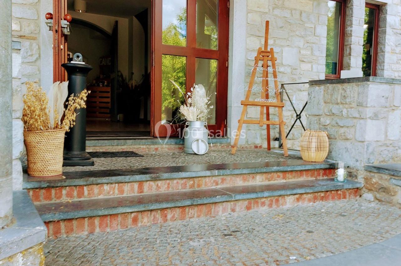 Entrée d'une maison avec des marches en pierre, décorée de paniers, fleurs séchées et un chevalet en bois.