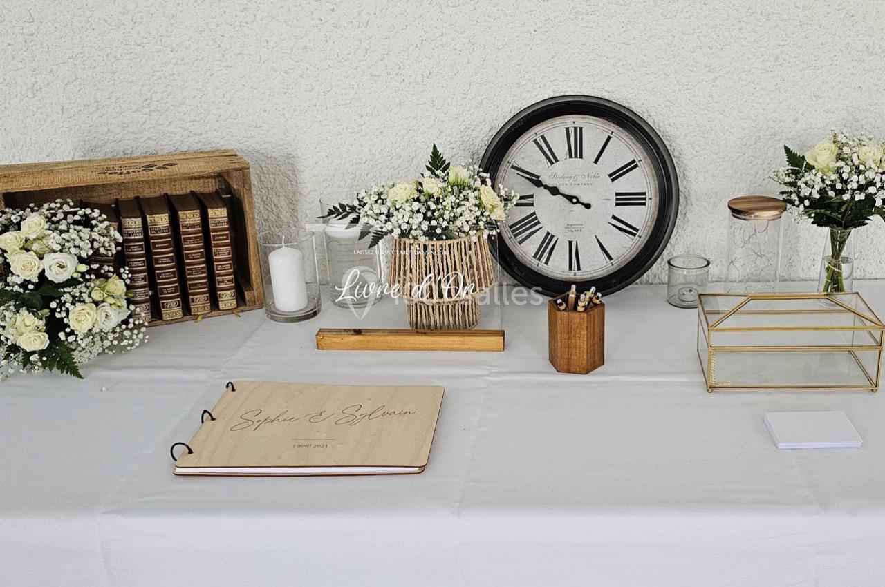 Table décorée avec des fleurs blanches, livres anciens, une horloge, un carnet en bois et divers accessoires.